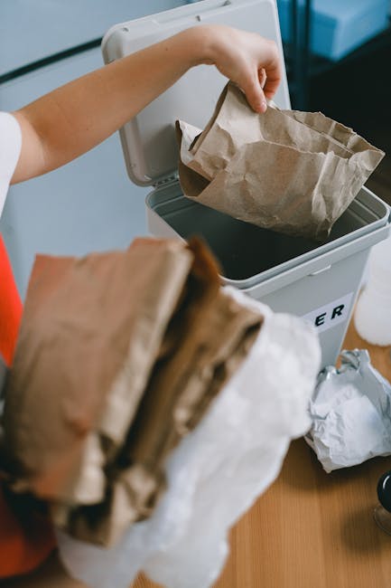 Close-up image of several black plastic rubbish bags filled with waste, tied securely at the top, and placed against a plain, light-colored wall. The bags appear to be made of shiny, crinkled plastic